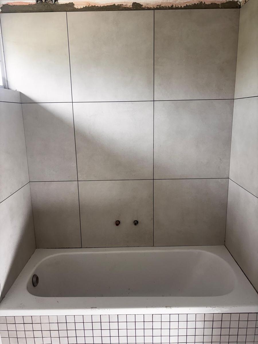 Ingebouwd ligbad met grote grijze wandtegels en mozaïek badrand