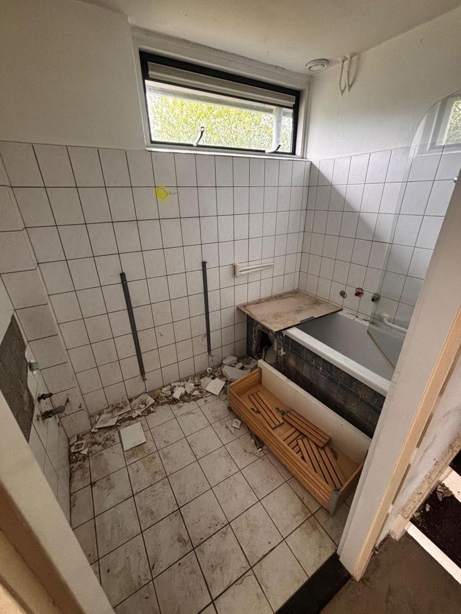 Oude badkamer tijdens de sloop, met verwijderde tegels en oud bad