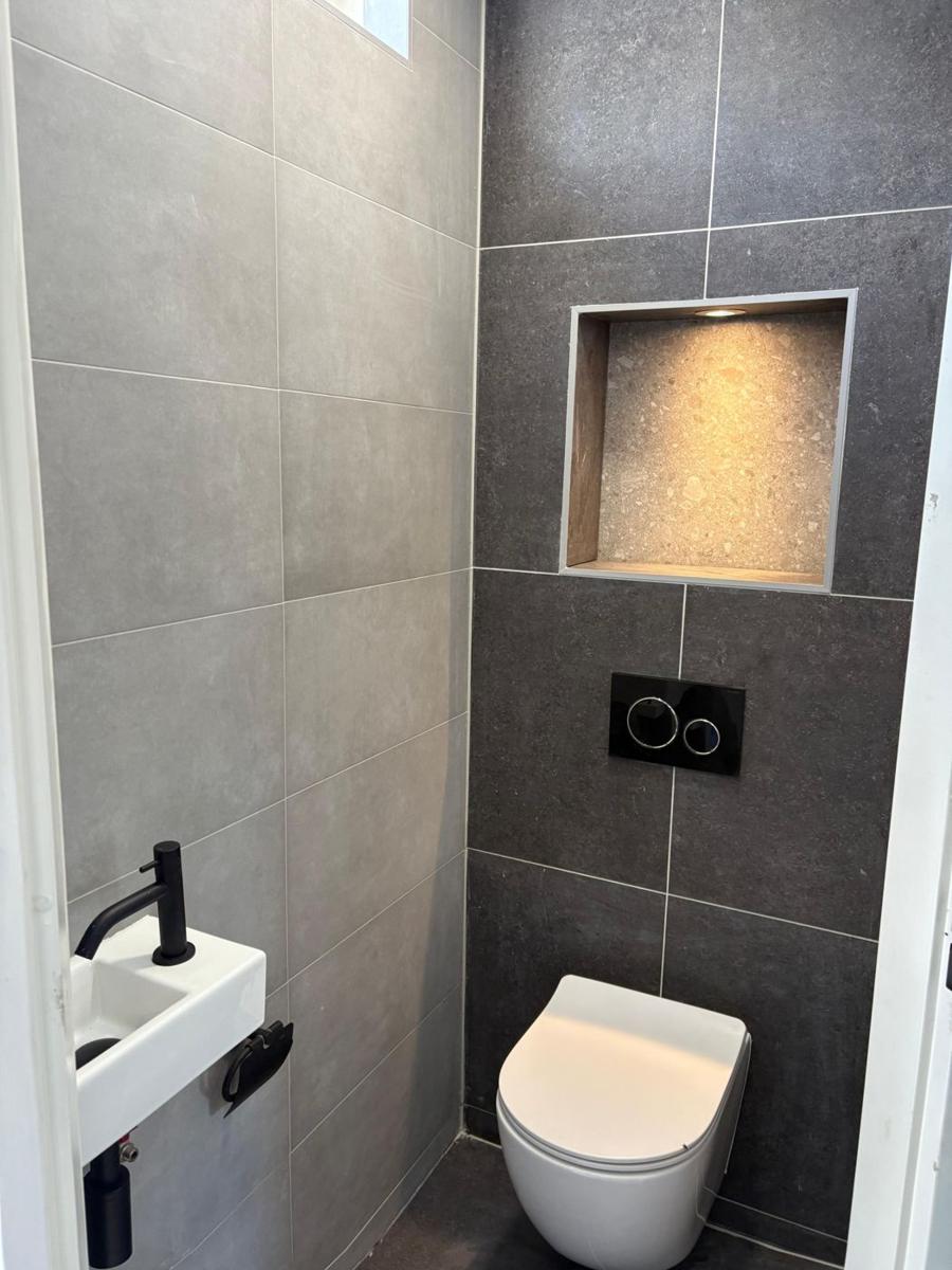 Door Tegel Fix gerenoveerd toilet met antracieten tegels, verlichte nis en zwart fonteinkraantje