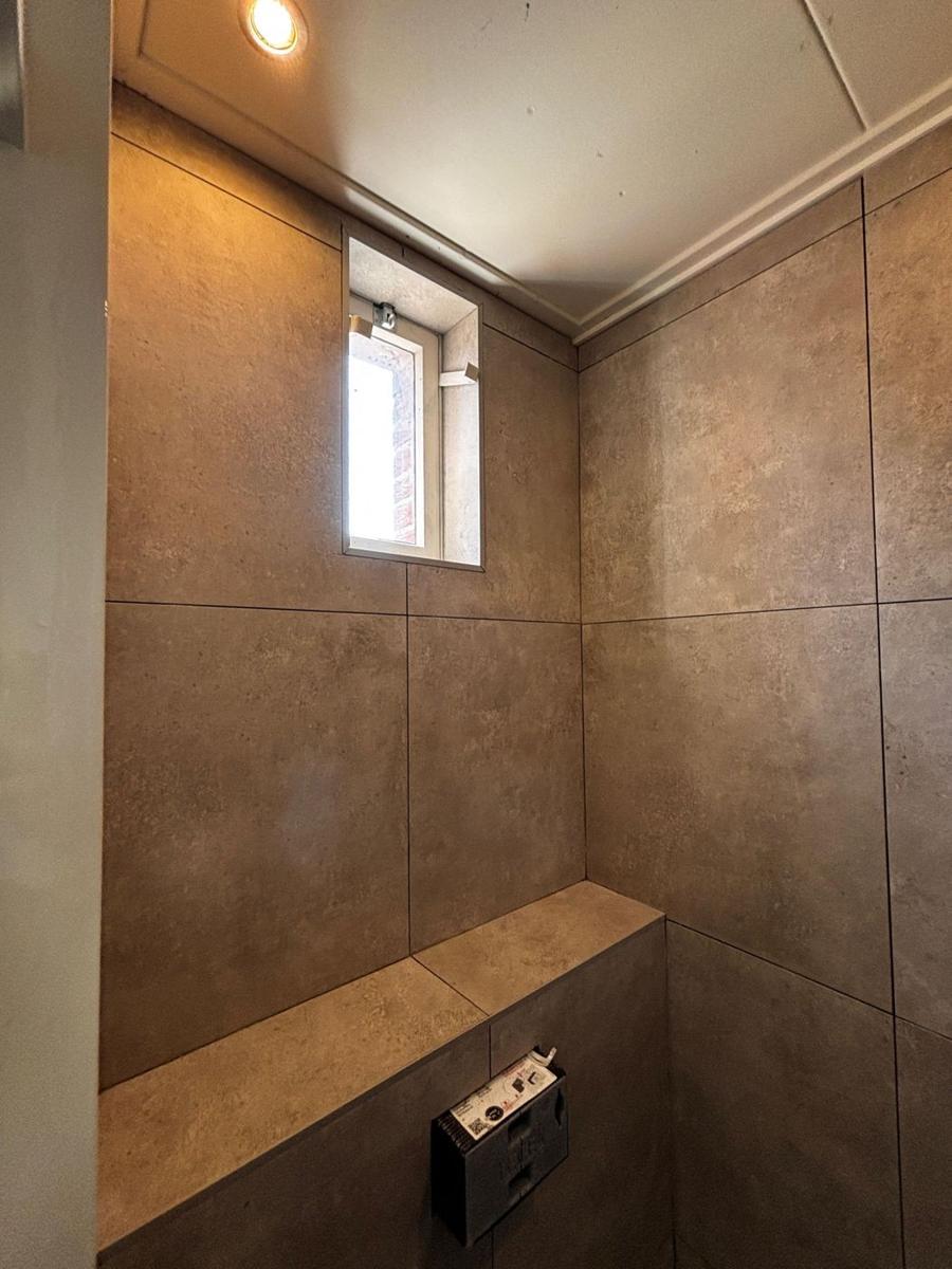 Toiletruimte met grote beige tegels, betegelde ombouw en raam